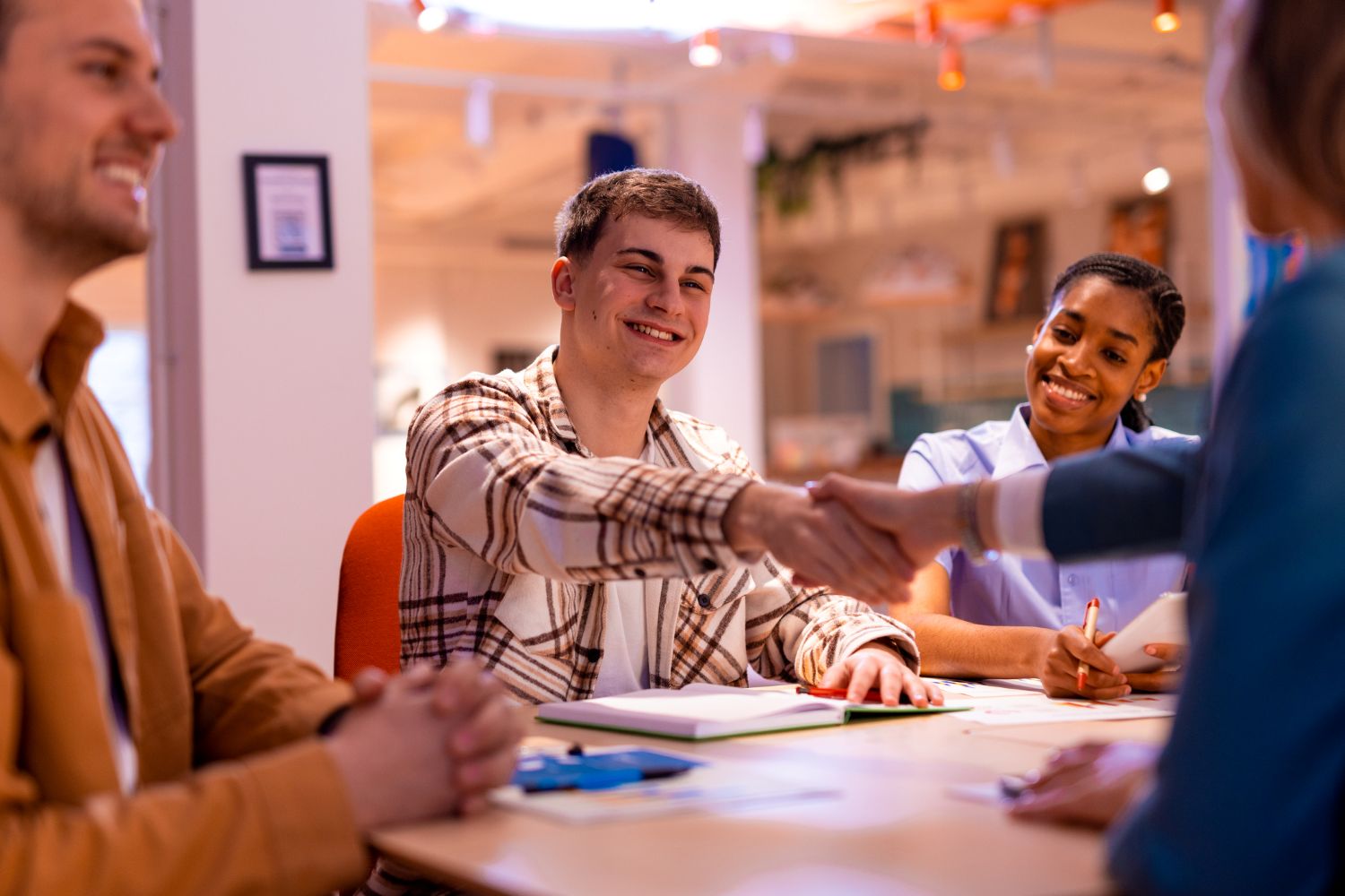 People gathered around a table during a meeting, with two participants shaking hands.